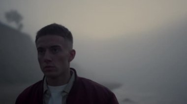 Deniz sahilinde yürüyen ciddi bir adam. Hüsrana uğramış adam sisli kıyıda duruyor.