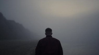 Deniz kıyısında yürüyüş yapan şık bir adam. Üzgün adam okyanus ufkuna bakıyor