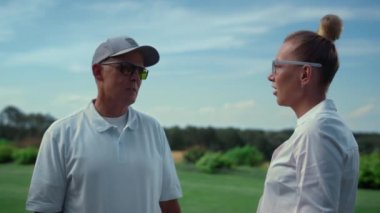 Birkaç golf oyuncusu çim sahada konuşuyor. Golfçüler yaz günü sohbet eder..