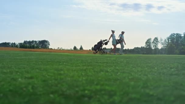 Golf players walk field on course. Golfing couple hold equipment clubs outside. — Vídeos de Stock
