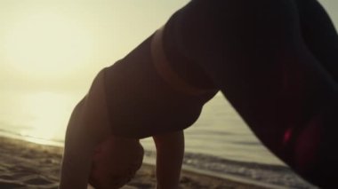 Formda sporcu kadın vücudunu büküyor kumlu sahilde yoga yaparken asana gibi duruyor.. 