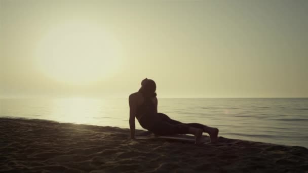 Silhuett yoga kvinna utövar på stranden. Flexibel tjejträning vid solnedgång. — Stockvideo