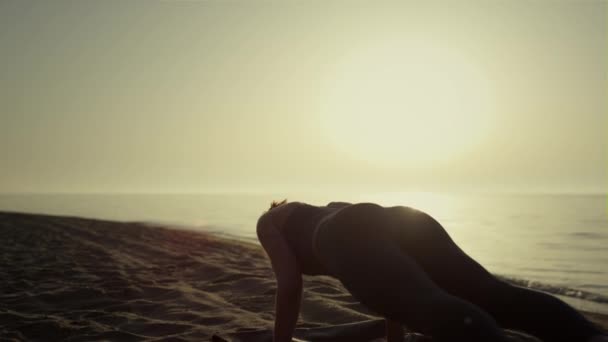 Sportos lány edz jógát a homokos parton. Nő csinál deszka pózol naplementekor — Stock videók