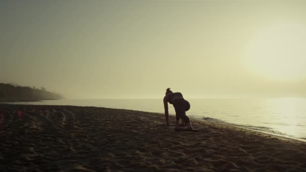 A jógás nő deszkás pózban emeli fel a kezét. A lány nyújtózkodik a homokos tengerparton — Stock videók