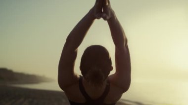 Sport girl raise hands up tilting body back at sunset. Woman practicing yoga.
