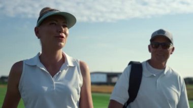 İki golfçü golf sahasında yürüyor. Gülümseyen çift dışarıda spor yapıyor..