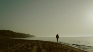 Siluet koşucusu kadın kumsalda antrenman yapıyor. Deniz kıyısında koşan sporcu kadın.