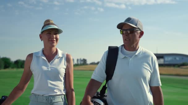 金持ちのカップルはゴルフスポーツを外で話している。2人のカントリークラブのメンバーがフェアウェイを歩く — ストック動画