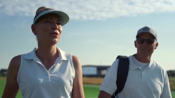 Two golf players walk country club course. Smiling couple talking sport outside. — Video Stock