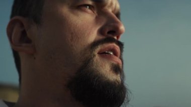 Akşam güneşini dört gözle bekleyen odaklanmış sakallı adamın portresi. Ciddi sporcu yüzünü kapat ve ağzını aç. Dışarıdaki su manzarasını izle. Orta yaşlı sporcu dışarıda dinleniyor, manzaranın tadını çıkarıyor.