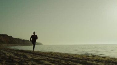 Atlet kız gün doğumunda koşuyor. Spor kıyafetleriyle kumsalda koşan tanınmayan bir kadın. Siluet güçlü sporcu kadın yaz sabahı deniz kıyısında koşuyor. Dışarıda yoğun kardiyo çalışması var..