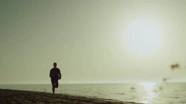 Güzel gün batımında deniz kıyısında koşan bir kadın silueti. Sakin deniz kenarında koşan atletik kız. Formda bir kadın yaz akşamı doğa üzerinde egzersiz yapıyor. Sağlıklı egzersiz.