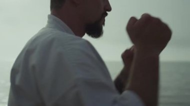 Brutal man exercising martial arts at sunset close up. Active sportsman practicing karate punches on beach. Bearded sporty guy training combat technique on evening sunlight. Sport healthy lifestyle.