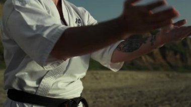 Tekvando ustası dışarıda Sandy Hills yakınlarında dövüş sanatları yapıyor. Kimonolu vahşi karate dövüşçüsü yaz akşamları dışarıda antrenman yapıyor. Sakallı adam savaş duruşu yapıyor. Spor sağlıklı yaşam tarzı.