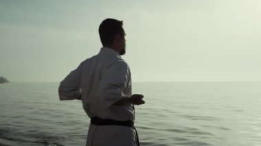 Gün batımında deniz kıyısında dövüş tekniğini mükemmelleştiren karate savaşçısı. Sakin atletik adam yaz akşamı kumsalda tekvando çalışıyor. Kimliği belirsiz sporcu dışarıda el egzersizi yapıyor..