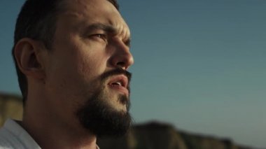 Düşünceli sporcu yüzü sahilde gün batımını yakından izliyor. Sakallı, güçlü bir adam doğa eğitiminden sonra dinleniyor. Deniz kenarında duran ciddi bir sporcunun portresi.. 