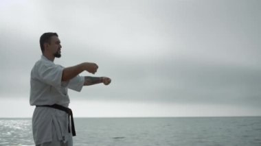 Sakallı sporcu sahilde kasvetli bir sabahta dövüş sanatları yapıyor. Kafkasyalı bir adam dışarıda karate öğreniyor. Deniz kıyısında dayanıklılık eğitimi veren ciddi bir sporcu. Spor etkinliği kavramı.