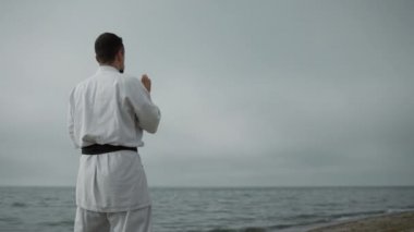 Bilinmeyen karate dövüşçüleri gündüz bulutlu havada saldırı talimi yapıyorlar. Aktif adam bulutlu gökyüzüne karşı deniz kenarında kumlu sahilde egzersiz yapıyor. Gün ışığında deniz kıyısında tanınmayan bir adam antrenman yapıyor..