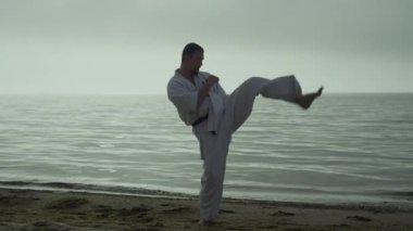 Kumsalda aktif tekme pratiği yapan bir atlet. Sakallı sporcu gün doğumunda dışarıda dövüş egzersizleri yapıyor. Güçlü adam yaz akşamları dışarıda dövüş eğitimi veriyor. Spor yaşam tarzı