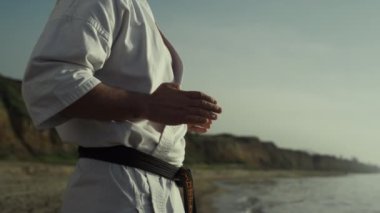 Bilinmeyen karate ustası deniz kıyısında dövüş egzersizleri yapıyor. Atletik adam gün batımında meditasyon tekniği eğitimi alıyor. Güçlü sporcu elleri doğada dövüş sanatları uyguluyor.. 