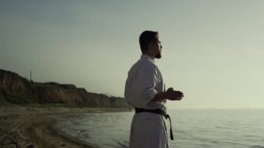 Vahşi bir sporcu kumlu sahil yaz akşamında meditasyon egzersizleri yapıyor. Karate dövüşçüsü gün batımında dövüş tekniğini mükemmelleştiriyor. Odaklanmış sporcu güneş ışığında dövüş sanatları çalışıyor..