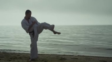 Sakallı sporcu gün batımında dışarıda saldırı talimi yapıyor. Karateci öğrenme tekmeleri