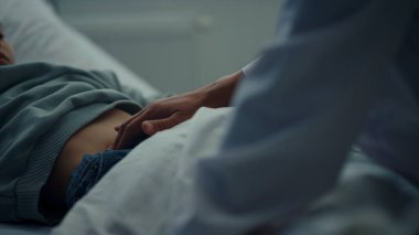 Doktor acil serviste karnına dokunuyor. Hasta çocuk yatakta yatıyor.