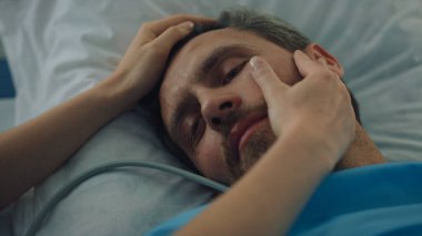 Cerrahi tedaviden sonra yatakta yatan yorgun bir hasta. Kadın elleri yüze dokunur