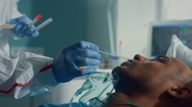 Hemşire koruyucu giysiyle ağız temizleme çubuğu alıyor. Eldivenler, bulaşıcı hastalıklar bölümü, yakın çekim..