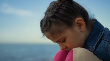 Sahilde deniz kenarında oturan utangaç çocuk. Küçük kız doğaya tepeden bakıyor.