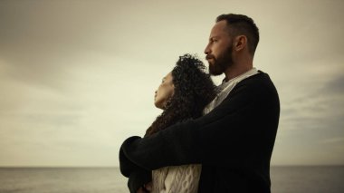 Aşıklar deniz sahillerinde gün batımının tadını çıkarıyor. Karma ırk çifti kıyıda kucaklaşıyor..
