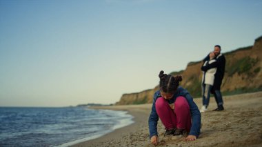 Aile deniz tatilinde sahilde vakit geçiriyor. Okyanusta kum oynayan küçük kız.