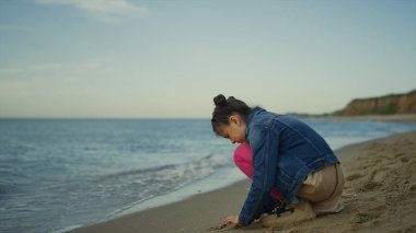 Çocuk deniz gezisinde kumsalda kum oynuyor. Küçük kız dışarıda tek başına vakit geçiriyor.