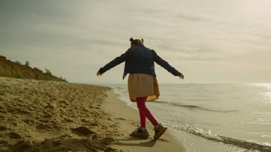 Gün batımında sahilde tek başına oynayan bir kız. Sevimli çocuk aile tatilinde eğleniyor.