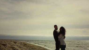 Sıradan kıyafetlerle ayakta duran deniz plajı çifti. Sevgililer tatilde sarılırlar.