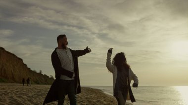 Sahilde gün batımında yürüyen neşeli bir çift. Aşıklar sahilde el ele tutuşmayı sever.