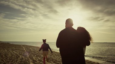 Güzel bir aile okyanus sahilinde gün batımına bakıyor. Anne baba çocuk güzel sahillerde yürüyor..