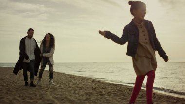 Rahat aile, tatil köyünün günbatımının tadını çıkarıyor. Anne ve babası okyanus kıyısında yürüyor.