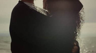 Deniz sahilinde birbirine sarılan iki kişi. Çift el etnik kıvırcık saçlara dokunur.