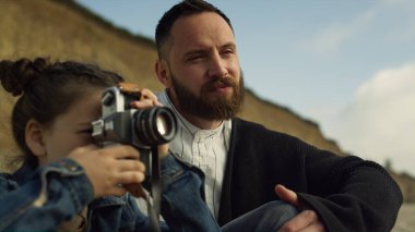 Küçük çocuk plaj tatilinde fotoğrafçılık oynuyor. Gülümseyen aile tatilde dinleniyor