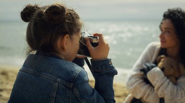Aile deniz tatilinde fotoğraf çeken küçük bir kız. Anne kız dışarıda kaynaşıyor..