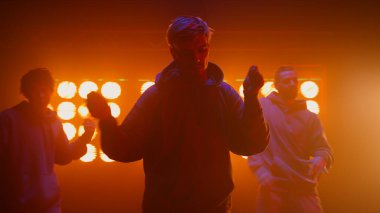 Sahne ışıkları altında sokak dansı yapan bir grup. Havalı takım ritmik hareket ediyor.