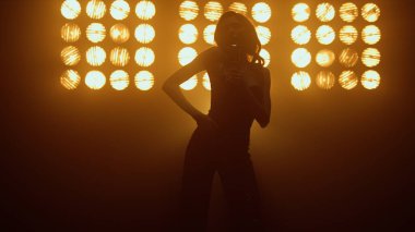 Siluet şarkı söyleyen kadın stüdyo ışıklarında mikrofonun yanında şehvetle dans ediyor.. 