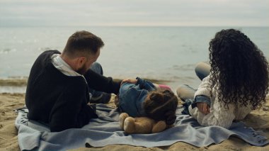 Anne ve babası deniz kıyısında plajda yatıyor. Mutlu aile piknikte oynuyor..