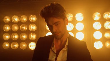 Sahne ışıkları altında geriye doğru hareket eden erkek model yaklaşıyor. Adam kulüp sahnesinde yürüyor..