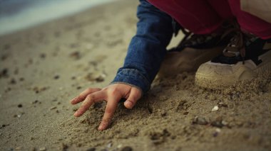 Çocuk elleri kum çiziyor. Genç kız deniz sahillerinde eğleniyor.