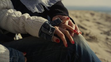 İnsanlar deniz kumu üzerinde dinlenen plaj ayakkabıları giyiyorlar. Romantik çift doğada buluşmanın tadını çıkarıyor..