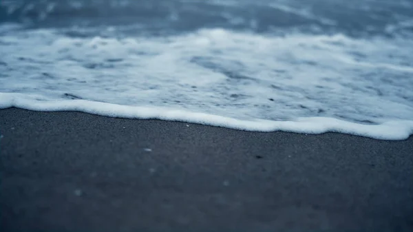 Onda branca a cair areia da praia. Superfície azul da água do mar salpicando na costa. — Fotografia de Stock