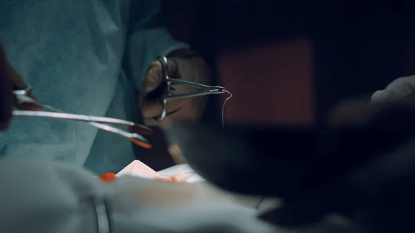 Doktor wykonuje operację z bliska. Narzędzia medyczne w ciemnej sali operacyjnej. — Zdjęcie stockowe