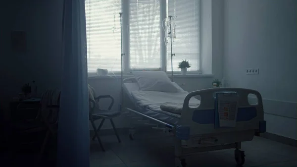 暗い空の病院の部屋のインテリア放棄されたきちんとしたベッドシャッター窓. — ストック写真